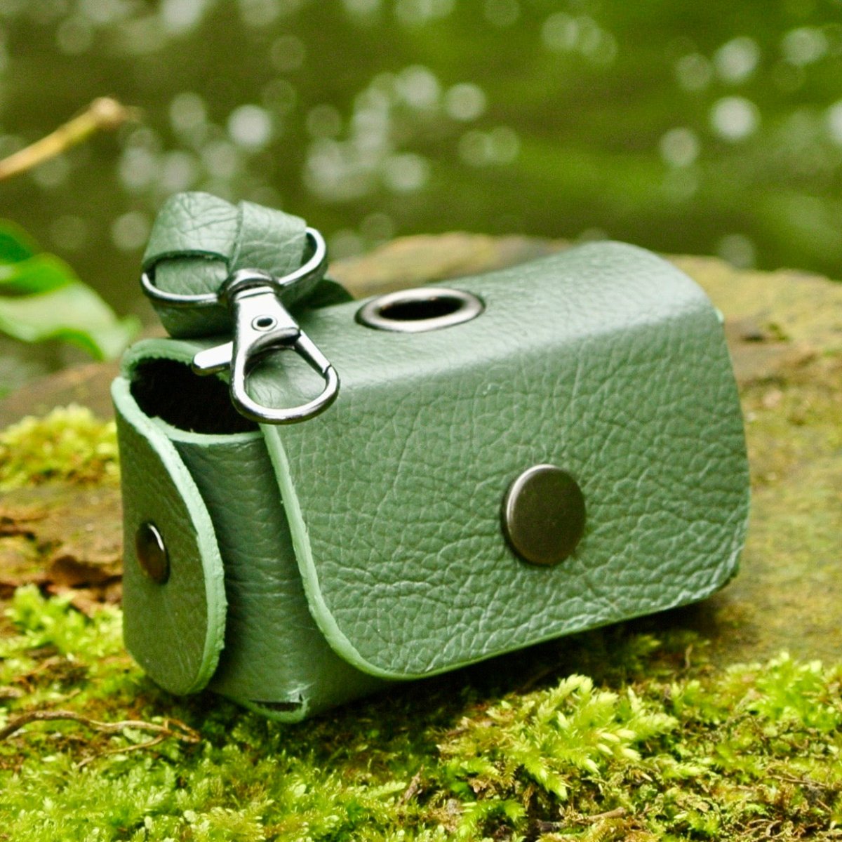 Green reclaimed leather dog waste bag holder photographed on moss